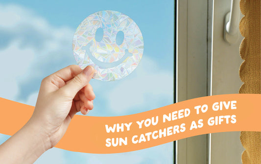 Why you need to give sun catchers as gifts. rainbow making sun catcher in smiley face shape is held by a feminine hand over a blue sky.